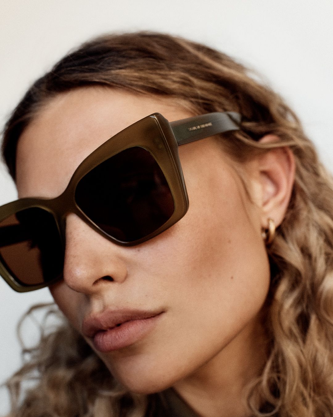 Close up of model's face wearing brown sunglasses with long curly blonde hair