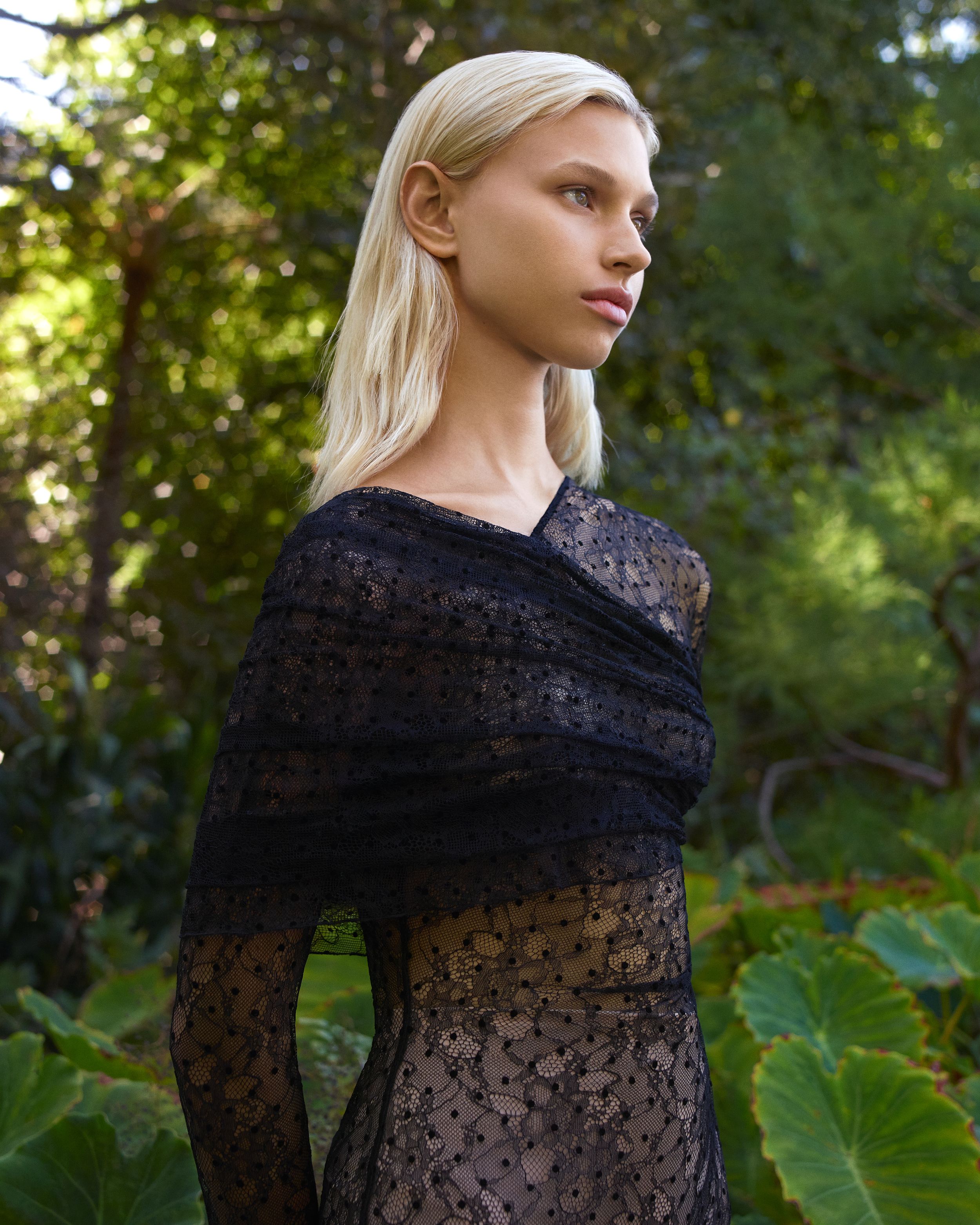 Midshot of model wearing a long-sleeved draped sheer lace dress