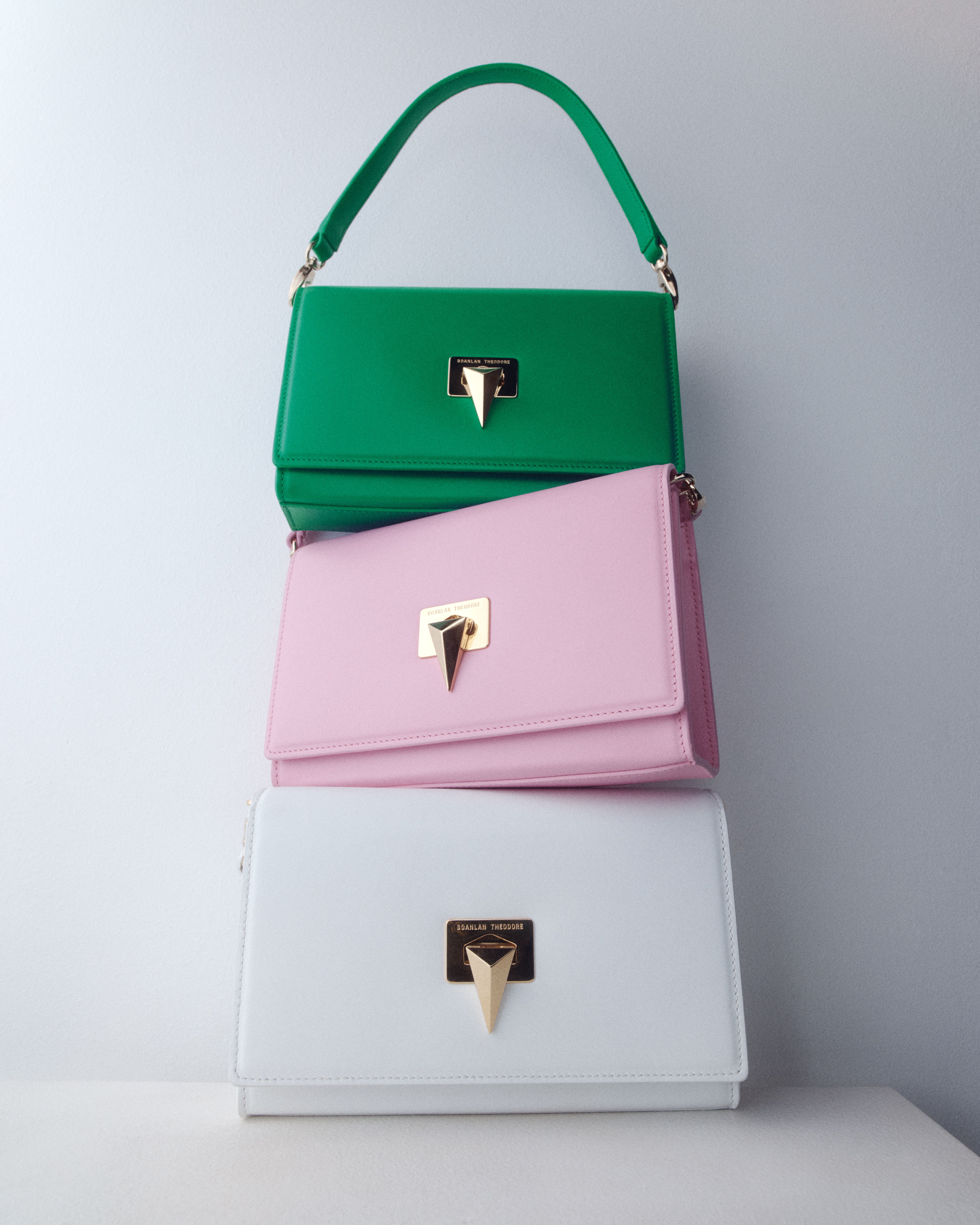 Three leather shoulder bags stacked on top of each other, with bright green at the top, light pink, then white