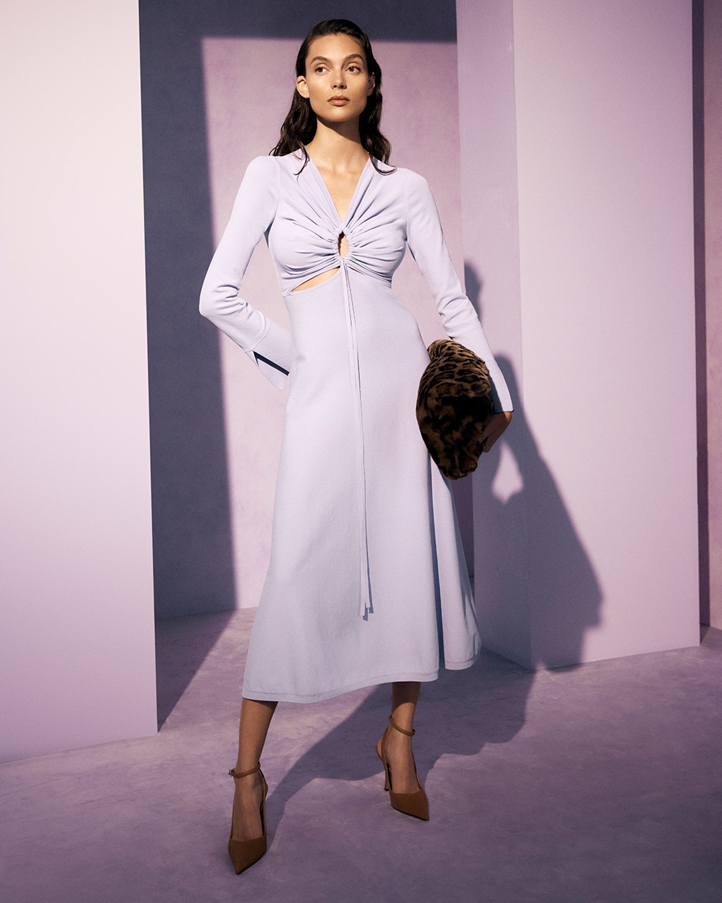 Brunette model wearing a lilac long-sleeve dress and faux fur clutch