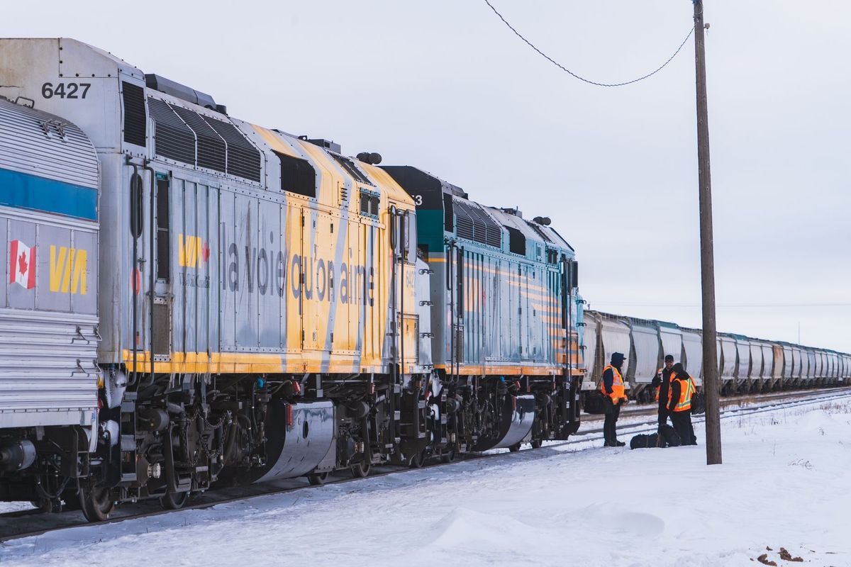 A VIA Rail Canada train stopped on snowy tracks with crew alongside