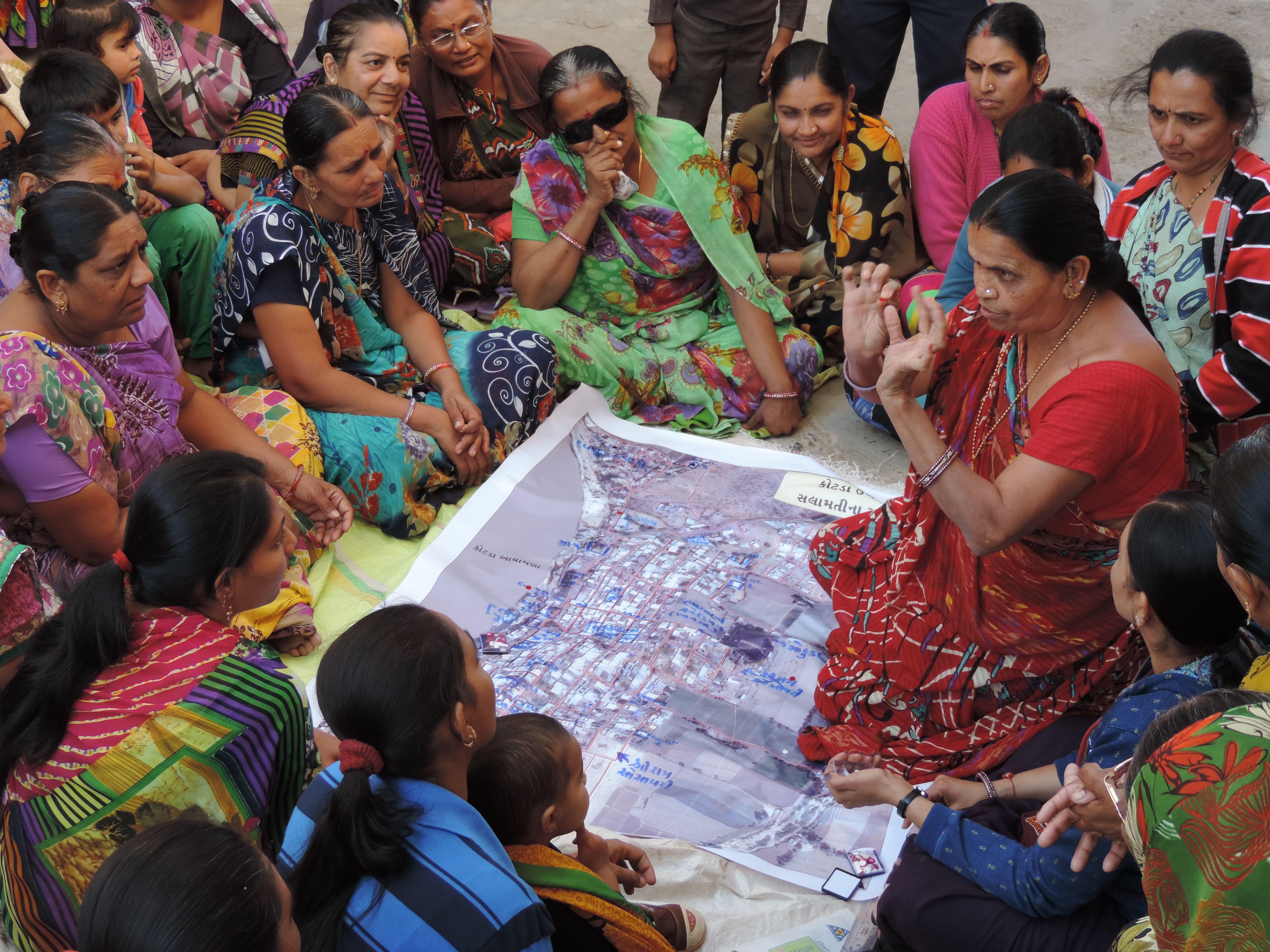 Women sit on the ground gathered around a map while one of them talks
