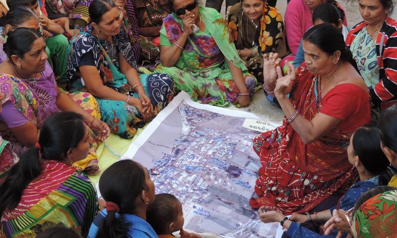 Women sit on the ground gathered around a map while one of them talks