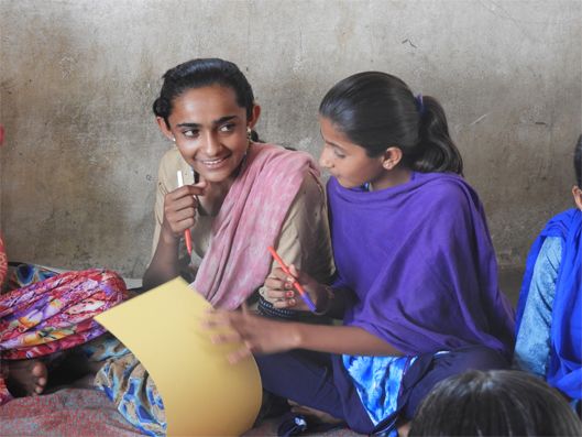 Two young girls are sitting together. One of them is smiling.