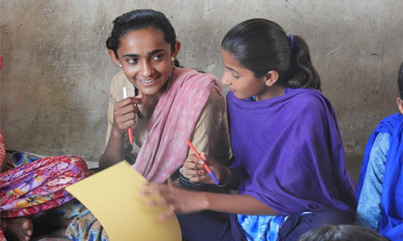 Two young girls are sitting together. One of them is smiling.