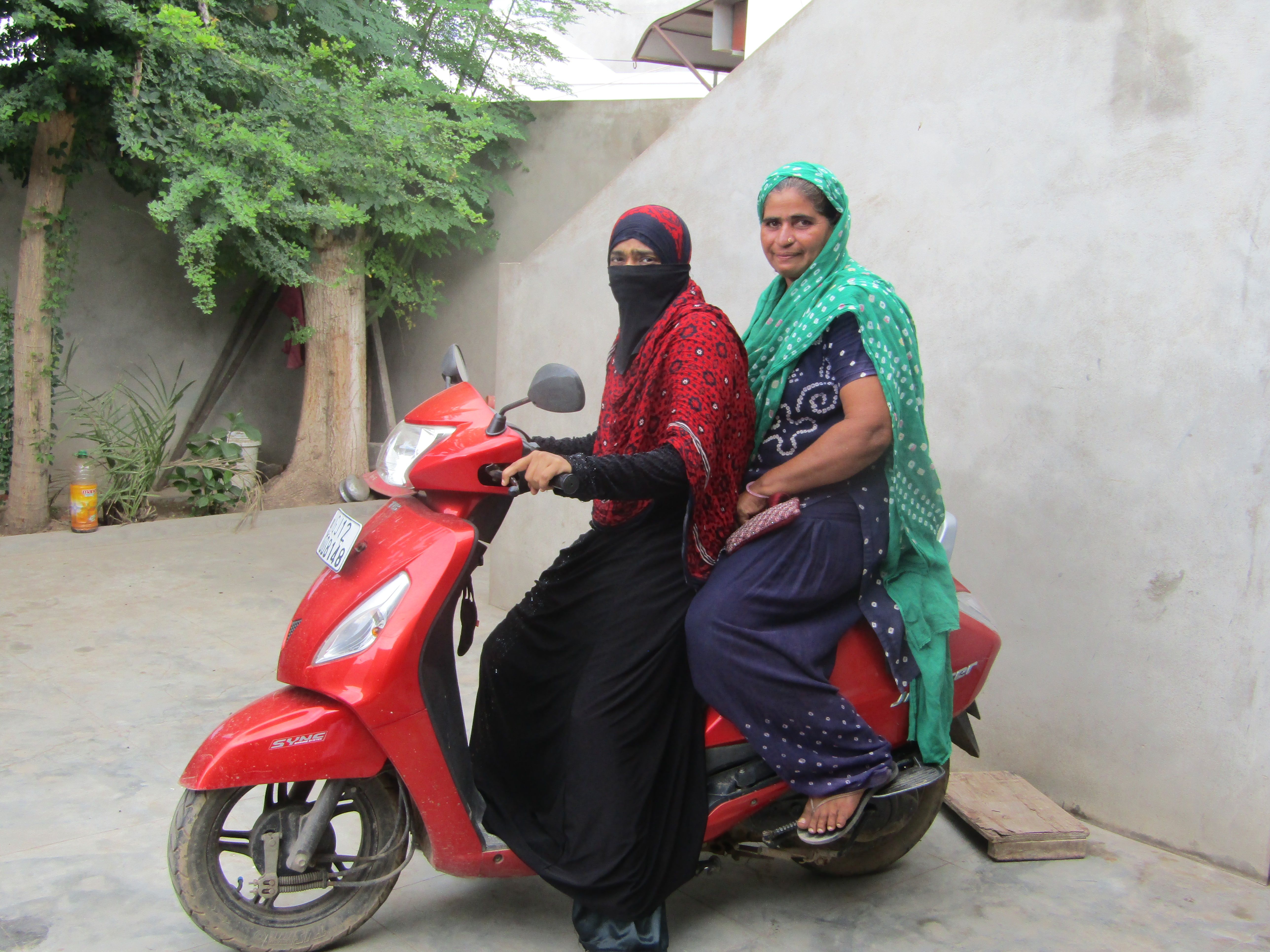 Two women sitting on a scooter and looking at the camera.