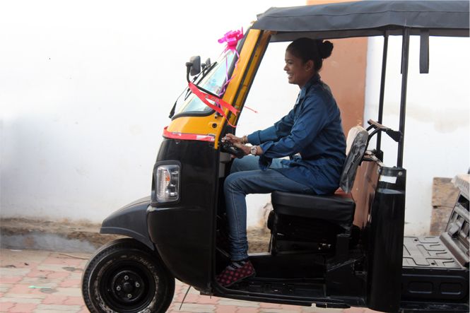 A woman is smiling and driving an auto rickshaw.