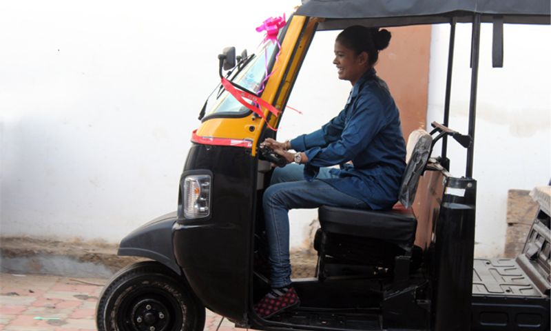 A woman is smiling and driving an auto rickshaw.