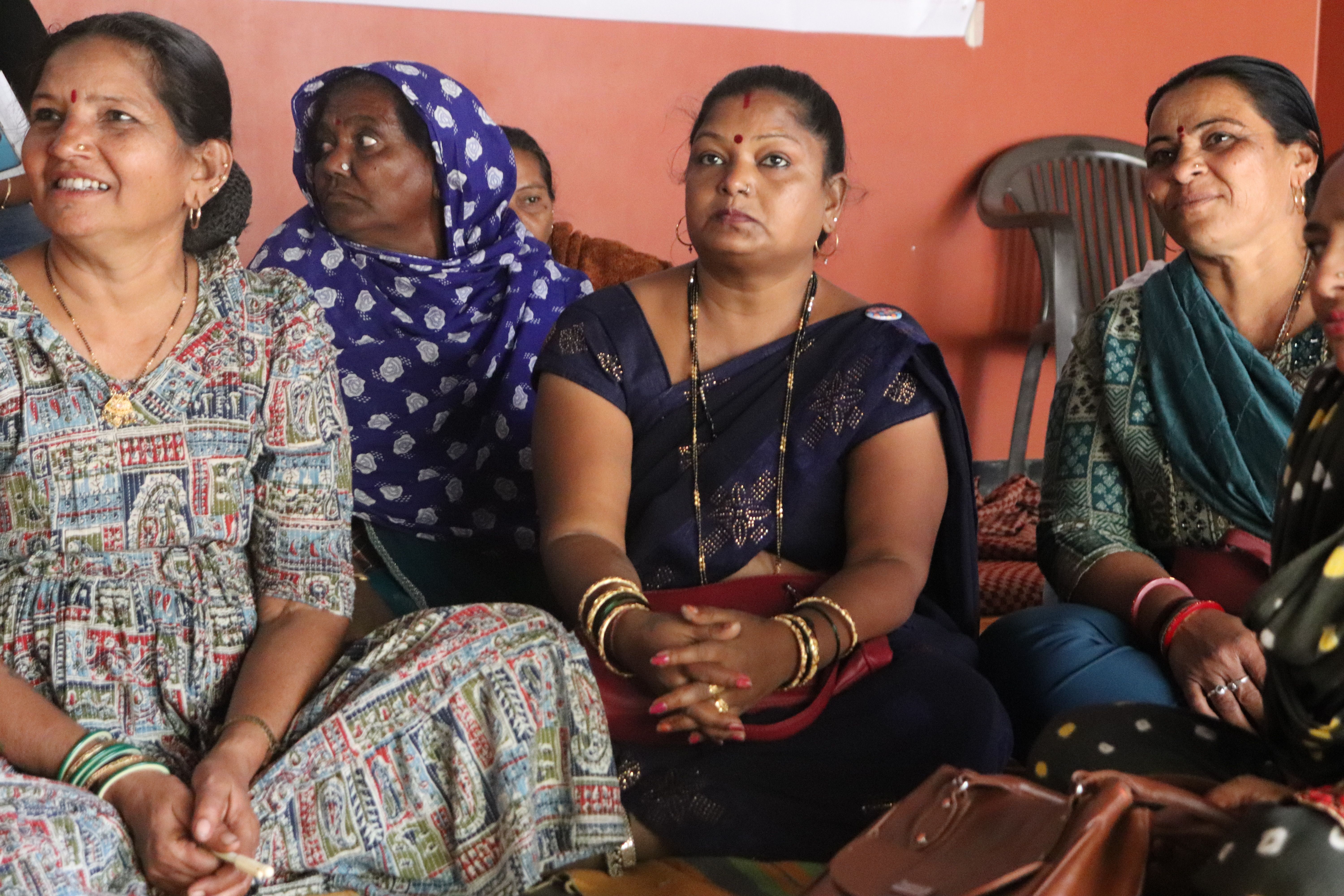 Woman wearing saree is holding a mic in front of an audiance