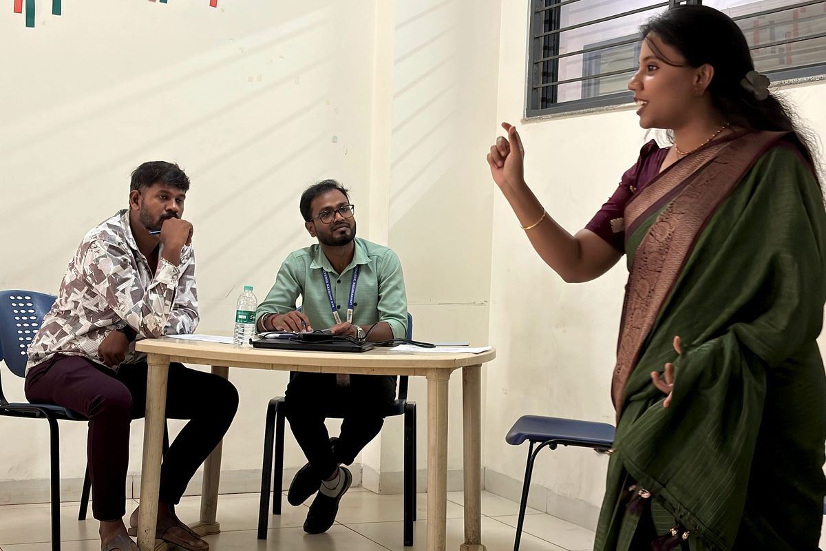 Ms. Sahana speaks to two participants seated at a table.