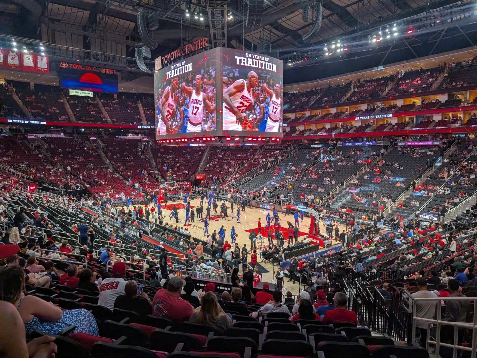 Pre-game warmups at Toyota Center in Houston. The jumbotron shows classic Rockets footage before tip-off.