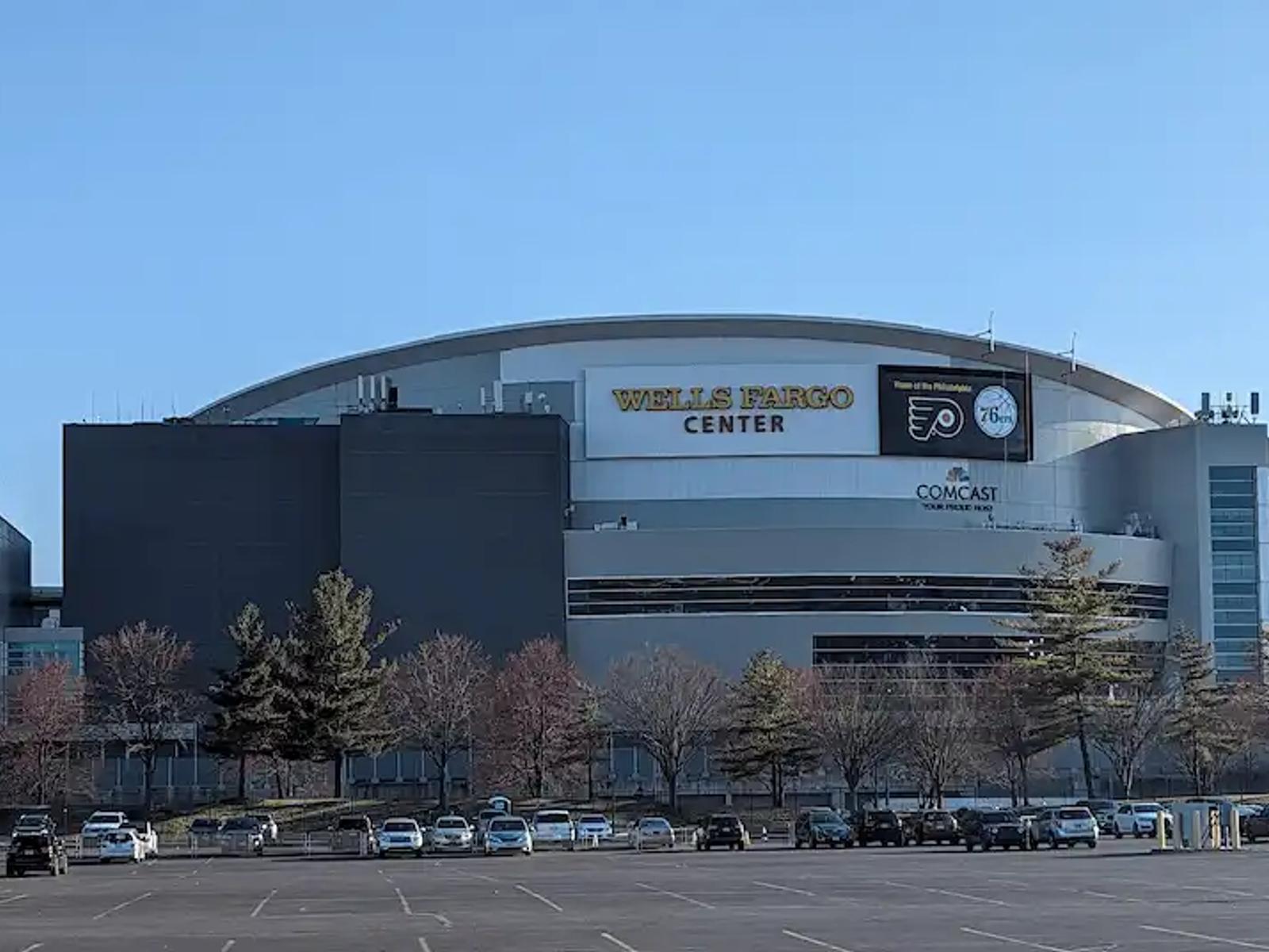 The exterior of the Wells Fargo Center in Philadelphia on a sunny day with a nearly empty parking lot.