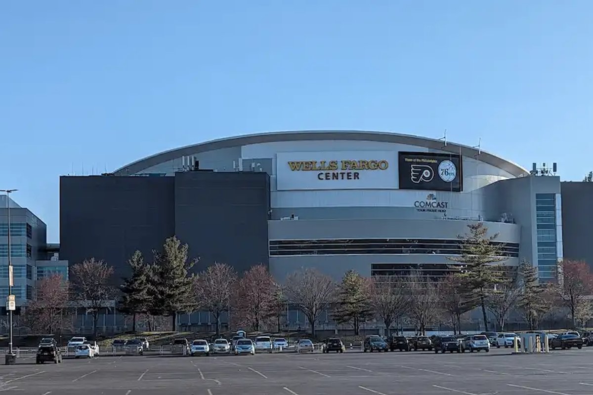 The exterior of the Wells Fargo Center in Philadelphia on a sunny day with a nearly empty parking lot.