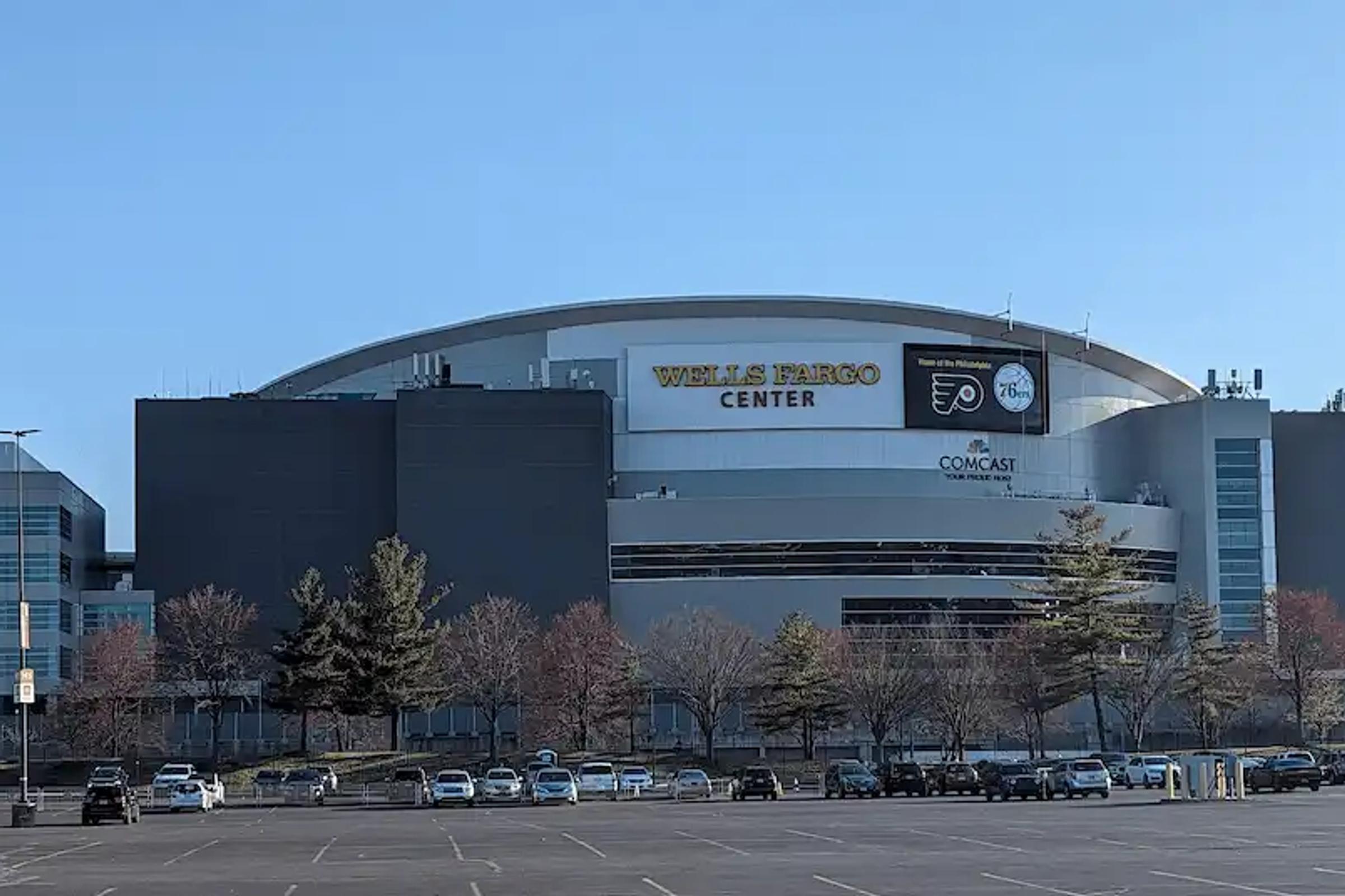 The exterior of the Wells Fargo Center in Philadelphia on a sunny day with a nearly empty parking lot.