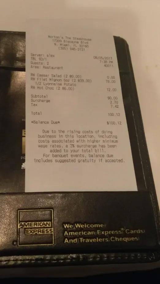 Morton's receipt in a check holder showing the salad, filet and hot chocolate cake with a 3% surcharge note.