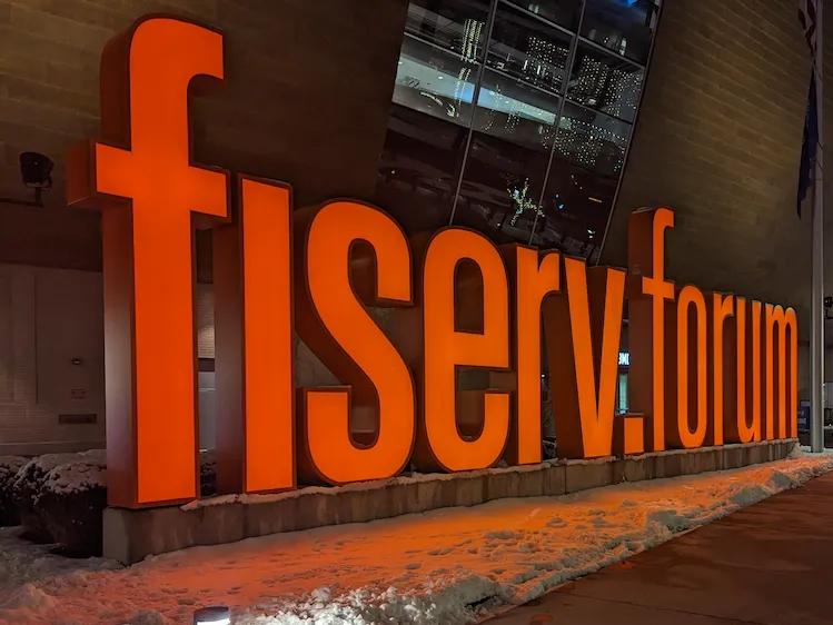 Bright orange Fiserv Forum sign glowing against the snowy sidewalk in Milwaukee.
