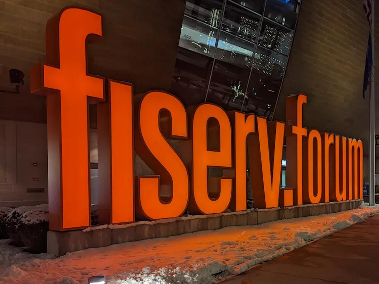 Bright orange Fiserv Forum sign glowing against the snowy sidewalk in Milwaukee.