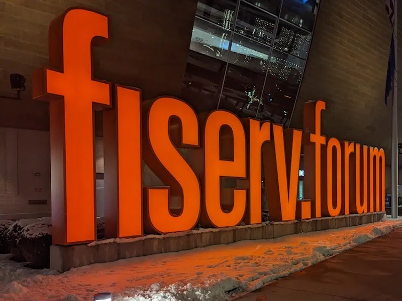 Bright orange Fiserv Forum sign glowing against the snowy sidewalk in Milwaukee.