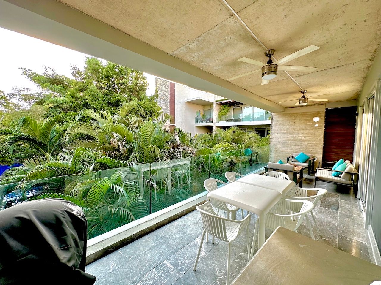 Terrace opening onto lush tropical vegetation and the Playacar building context at Vaivén del Mar