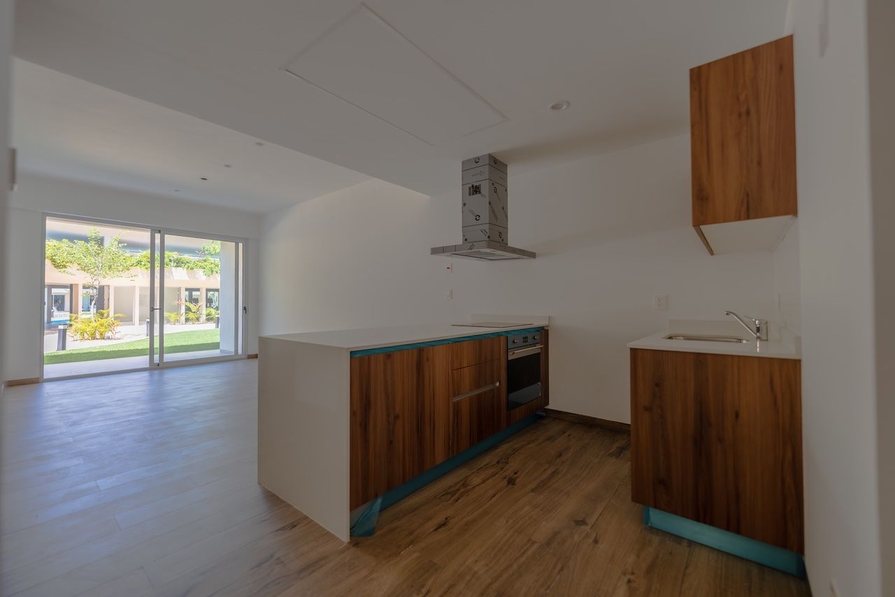 Open-plan kitchen with wood cabinetry and a sliding door open to greenery at The Leaf
