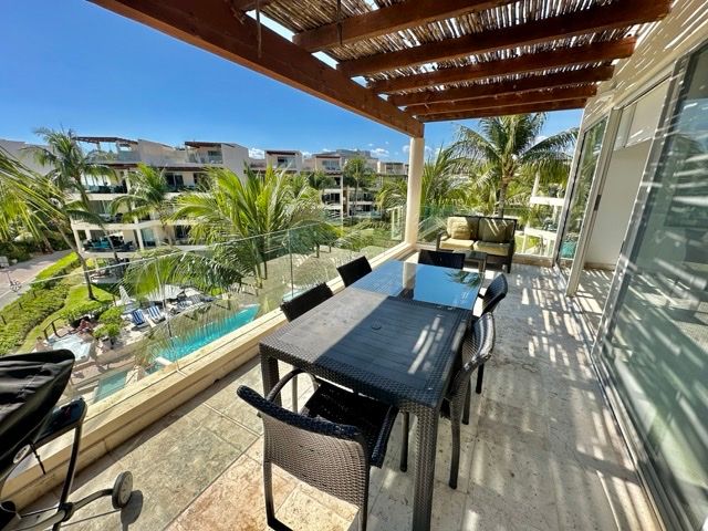 Covered terrace with a pergola and dining table overlooking the pool and palm trees at The Elements PH21