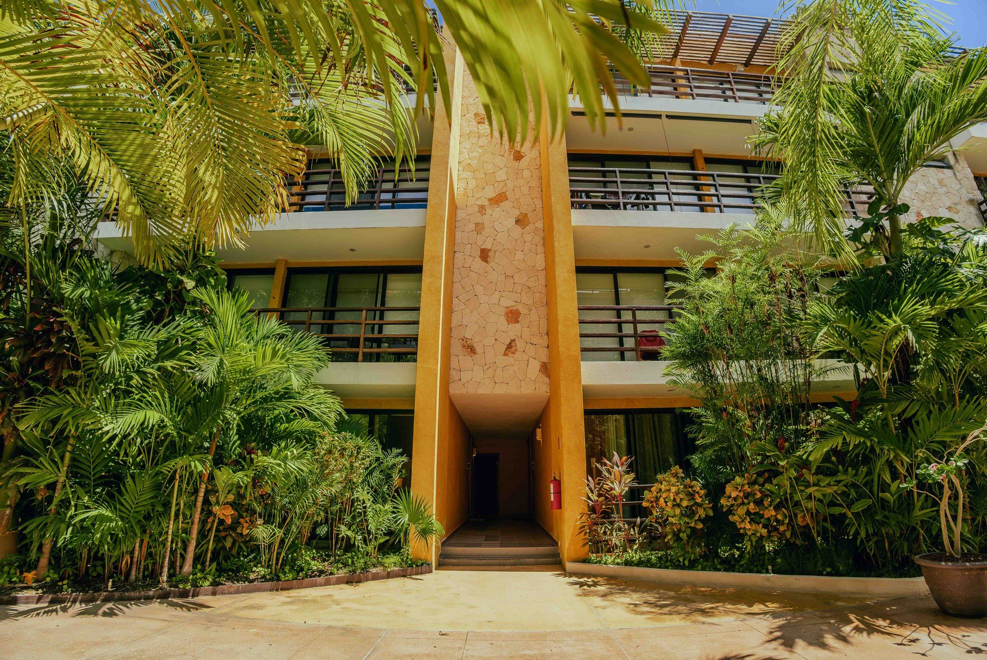 Building facade with balconies and a stone-clad entrance framed by palms at Lunada