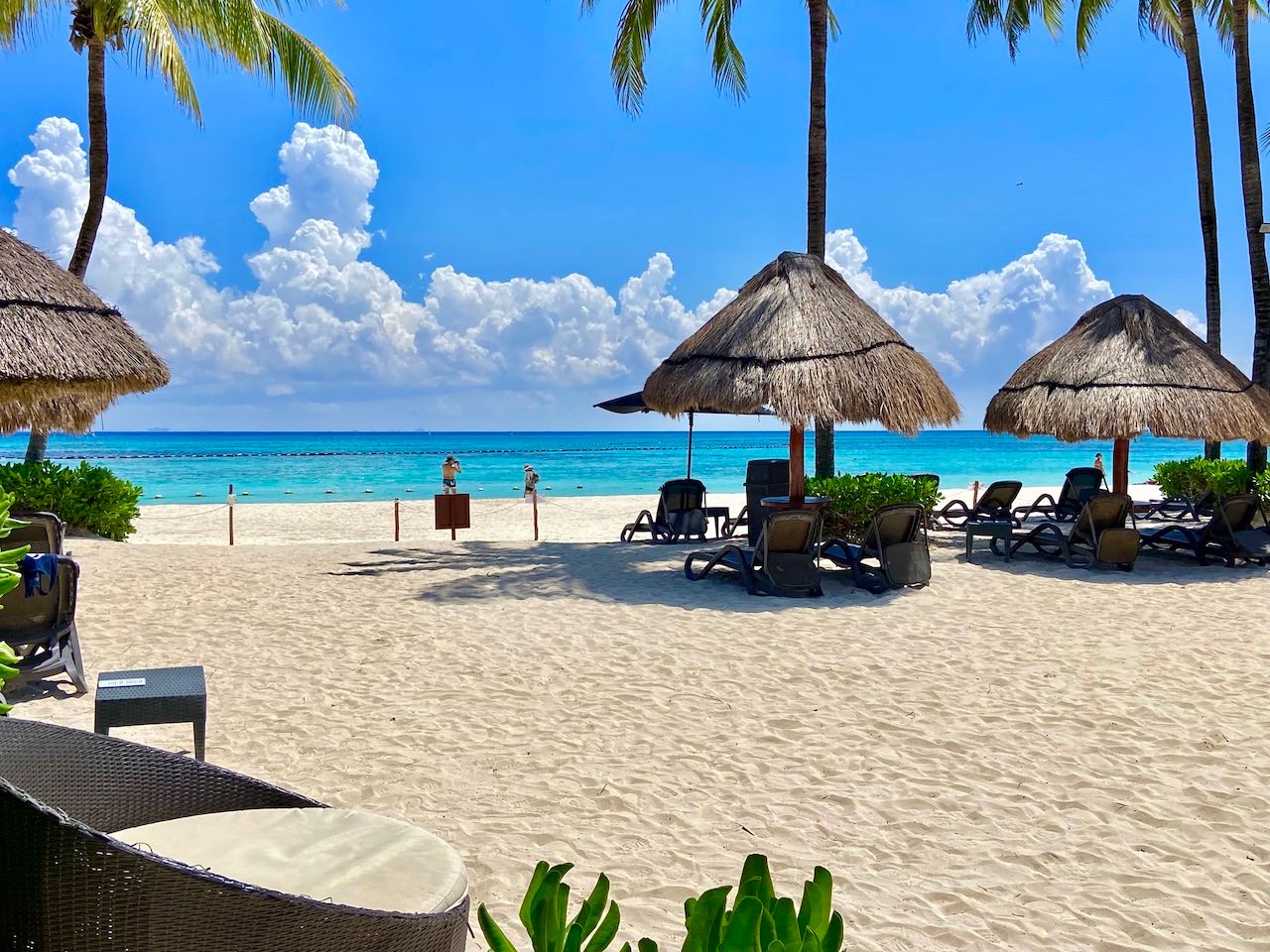 Beach with palapas, loungers and dramatic clouds over turquoise water at The Elements