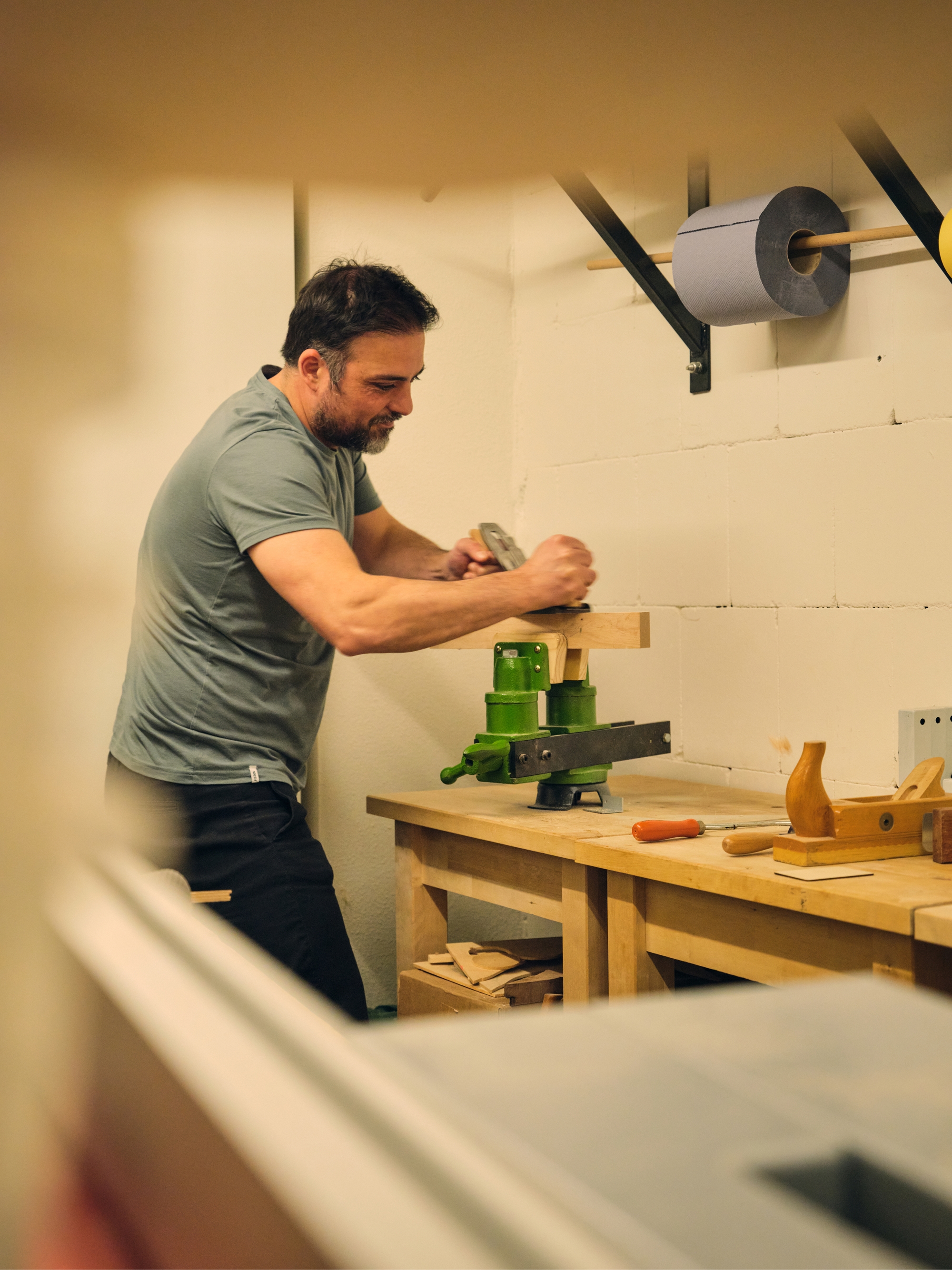 Person working with a vise and hand tools at a wooden workbench in a workshop