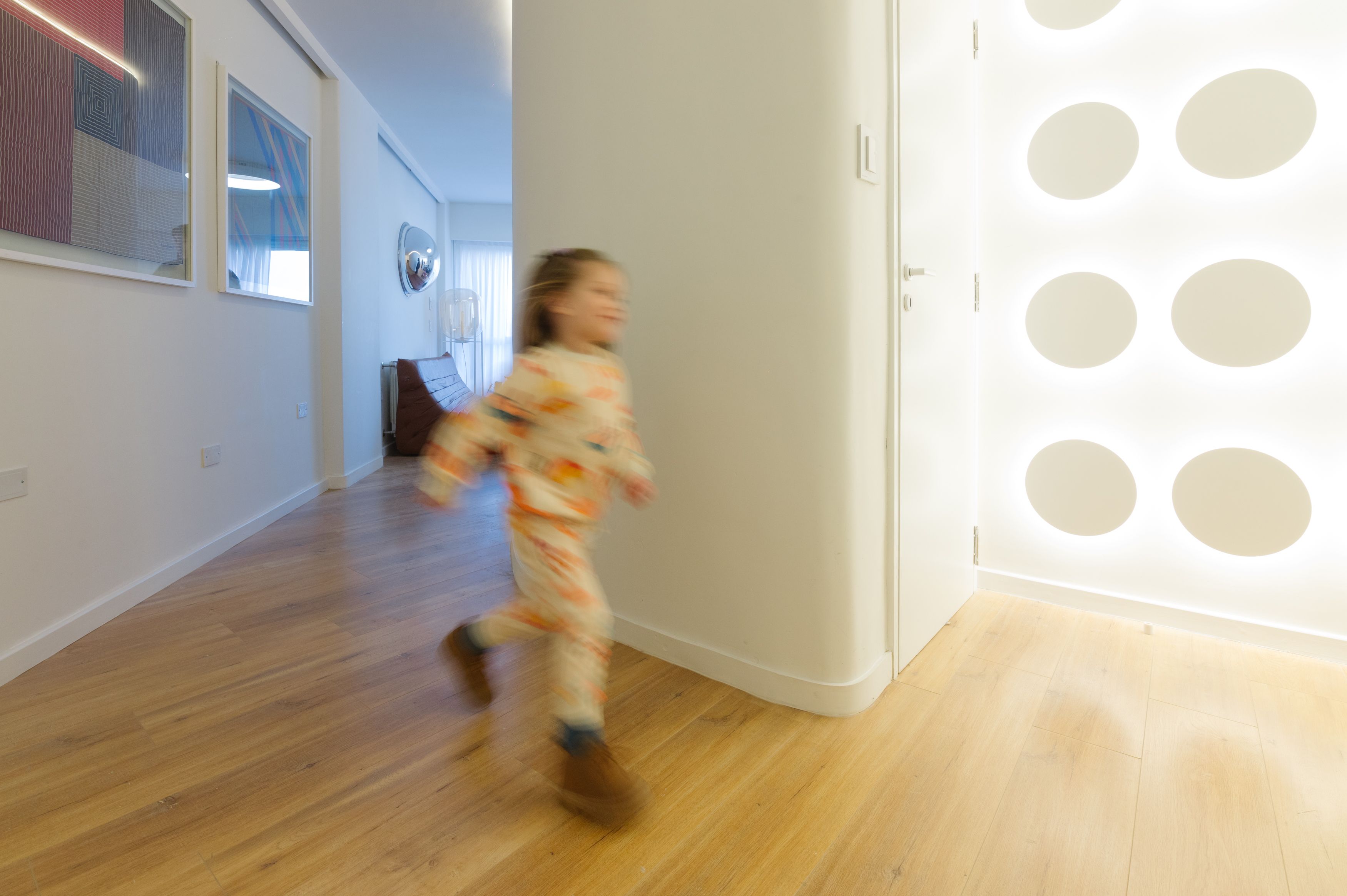 Niña corriendo por el pasillo del departamento Y485 en Córdoba, junto a una pared con luces circulares.