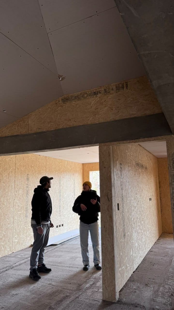 Dos personas recorren un interior en obra de PSMA, con paneles de OSB y cubierta inclinada.