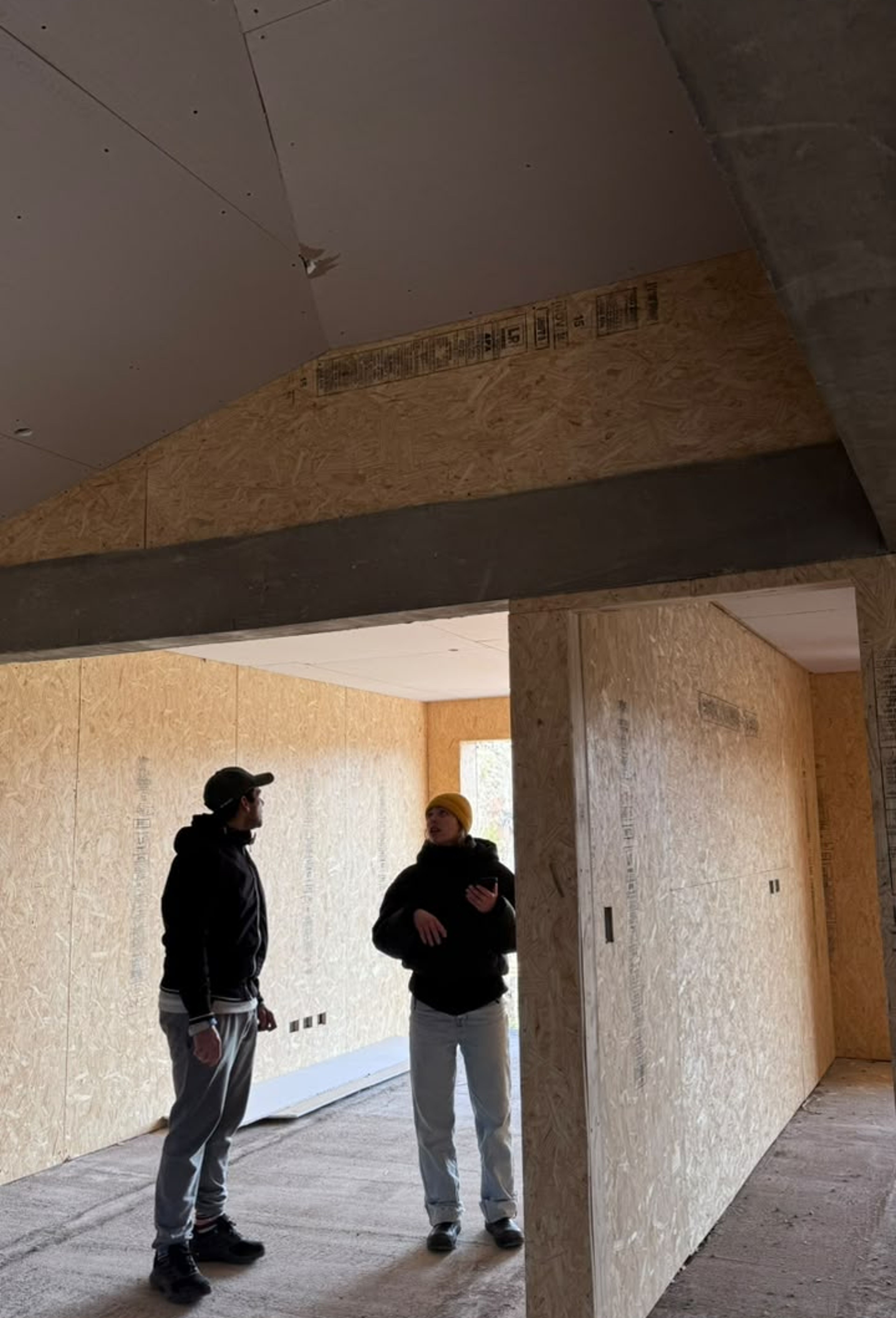 Dos personas recorren un interior en obra de PSMA, con paneles de OSB y cubierta inclinada.