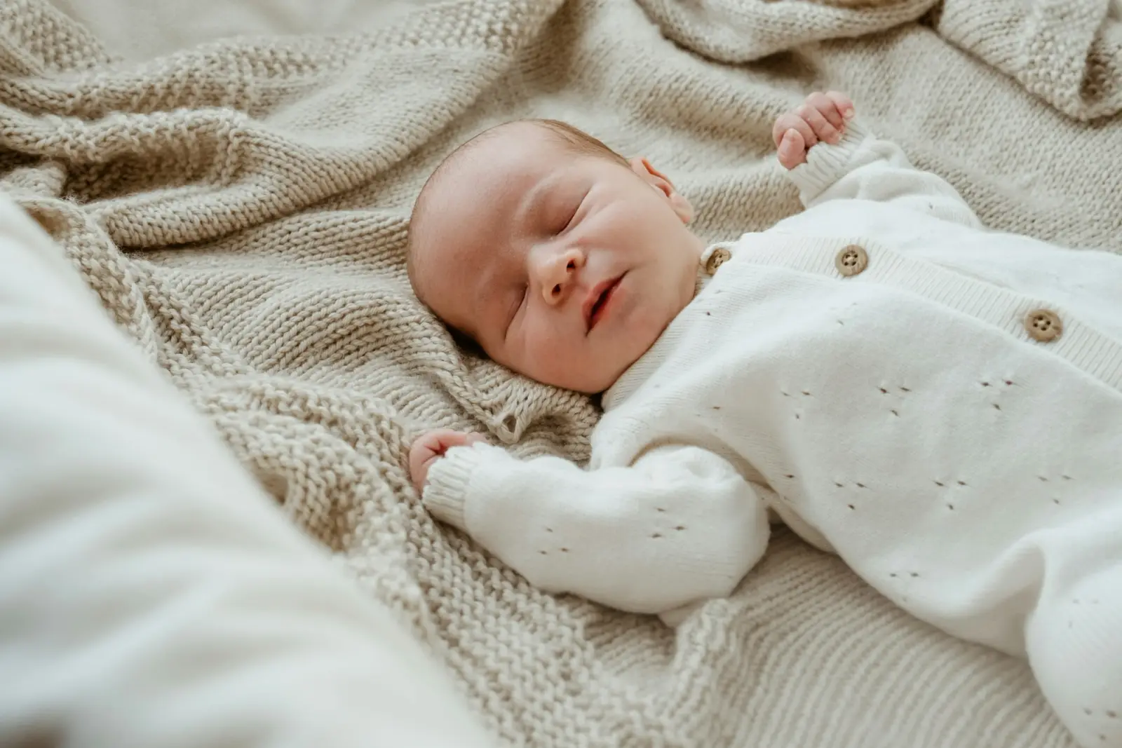 A newborn baby asleep on a knitted blanket