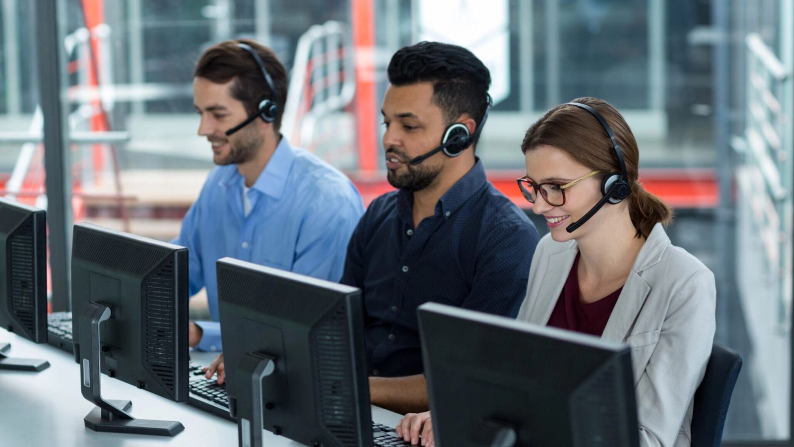 Smiling business executives with headsets using computers at desk in office