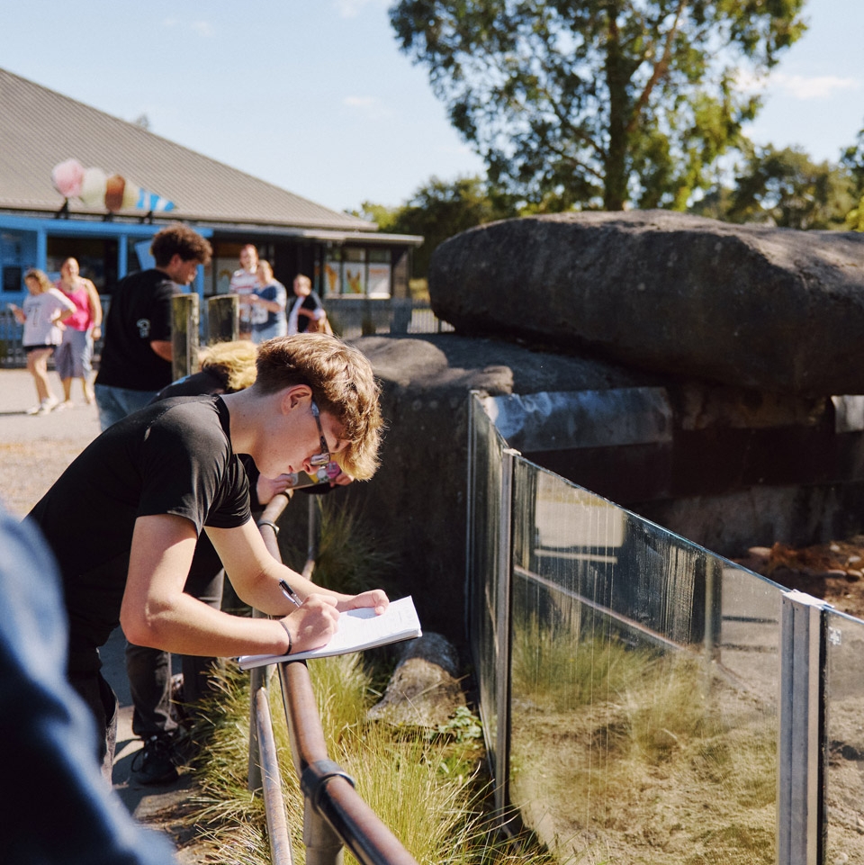 A student writing notes on a clipboard beside an enclosure