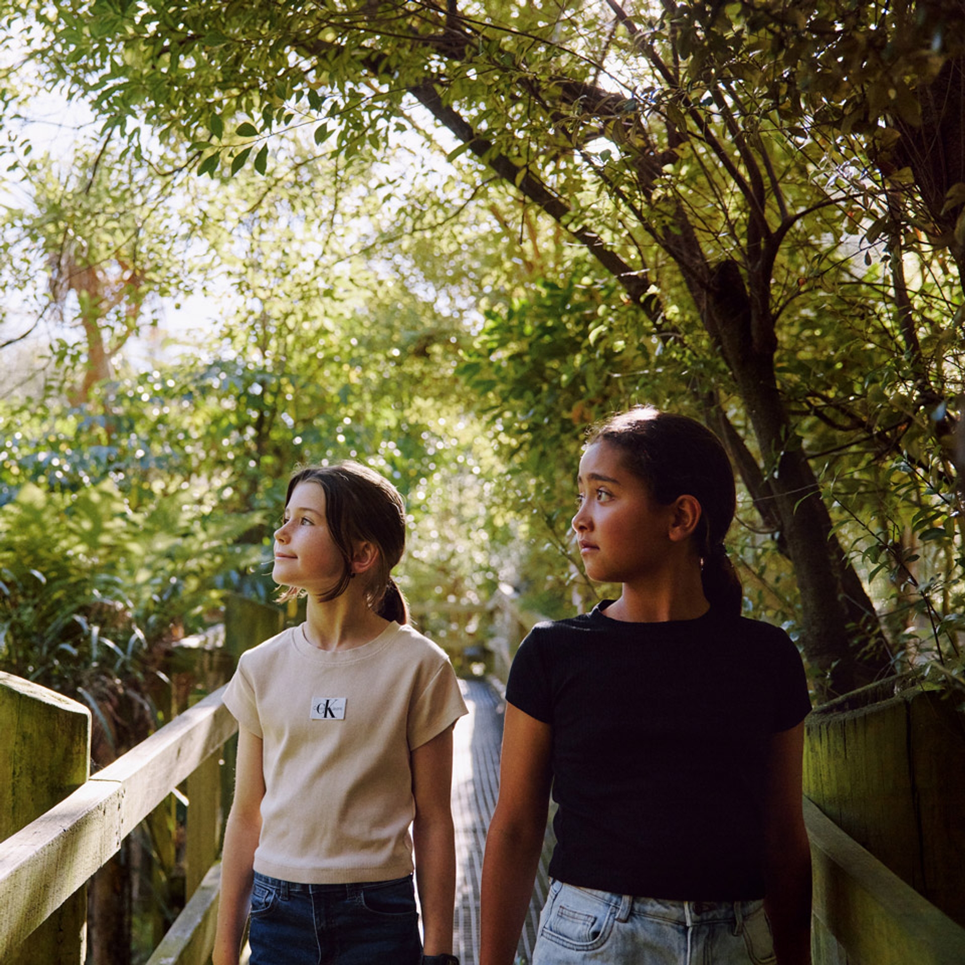 Two girls walking along a boardwalk through the trees