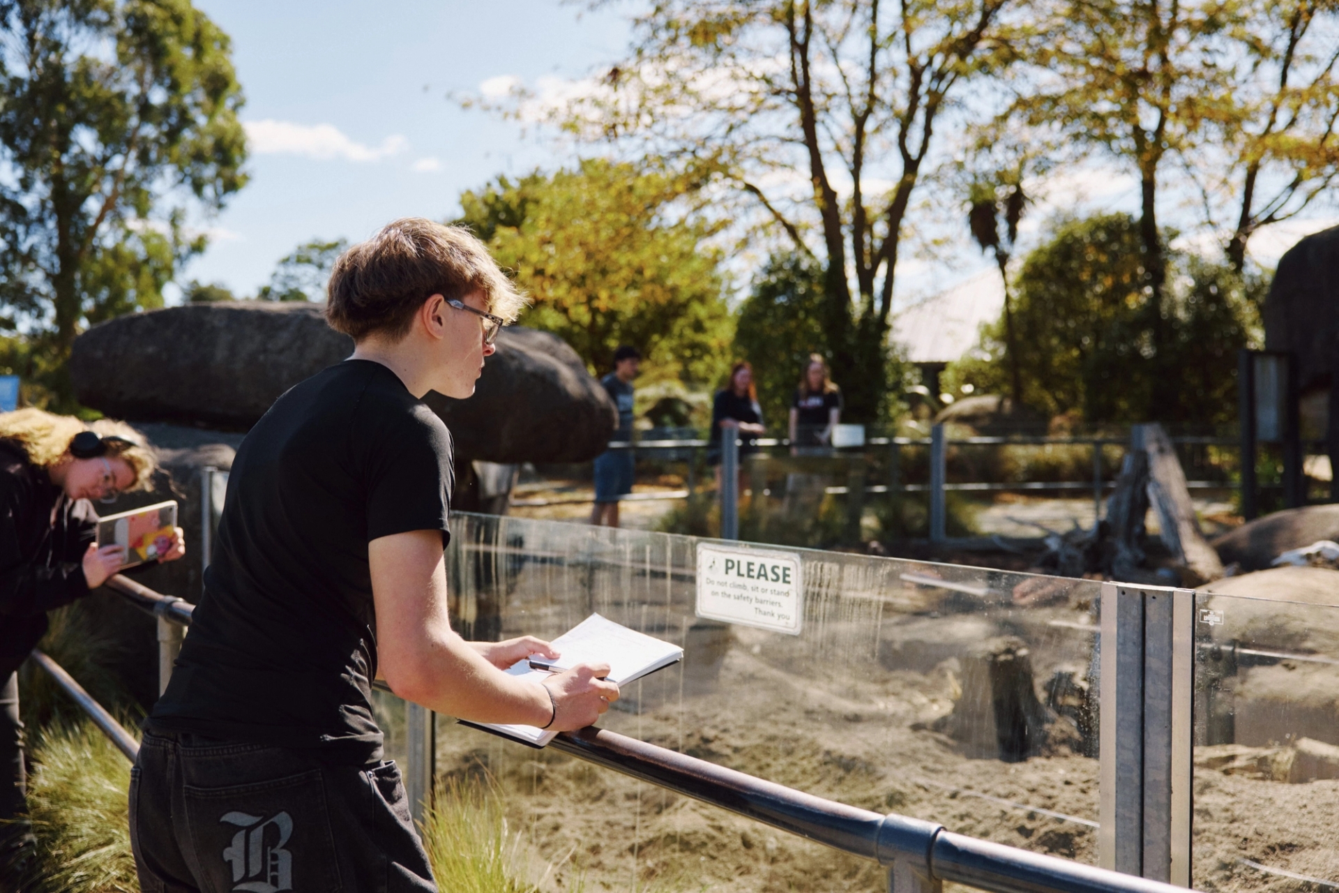 A student records observations on a clipboard beside an enclosure
