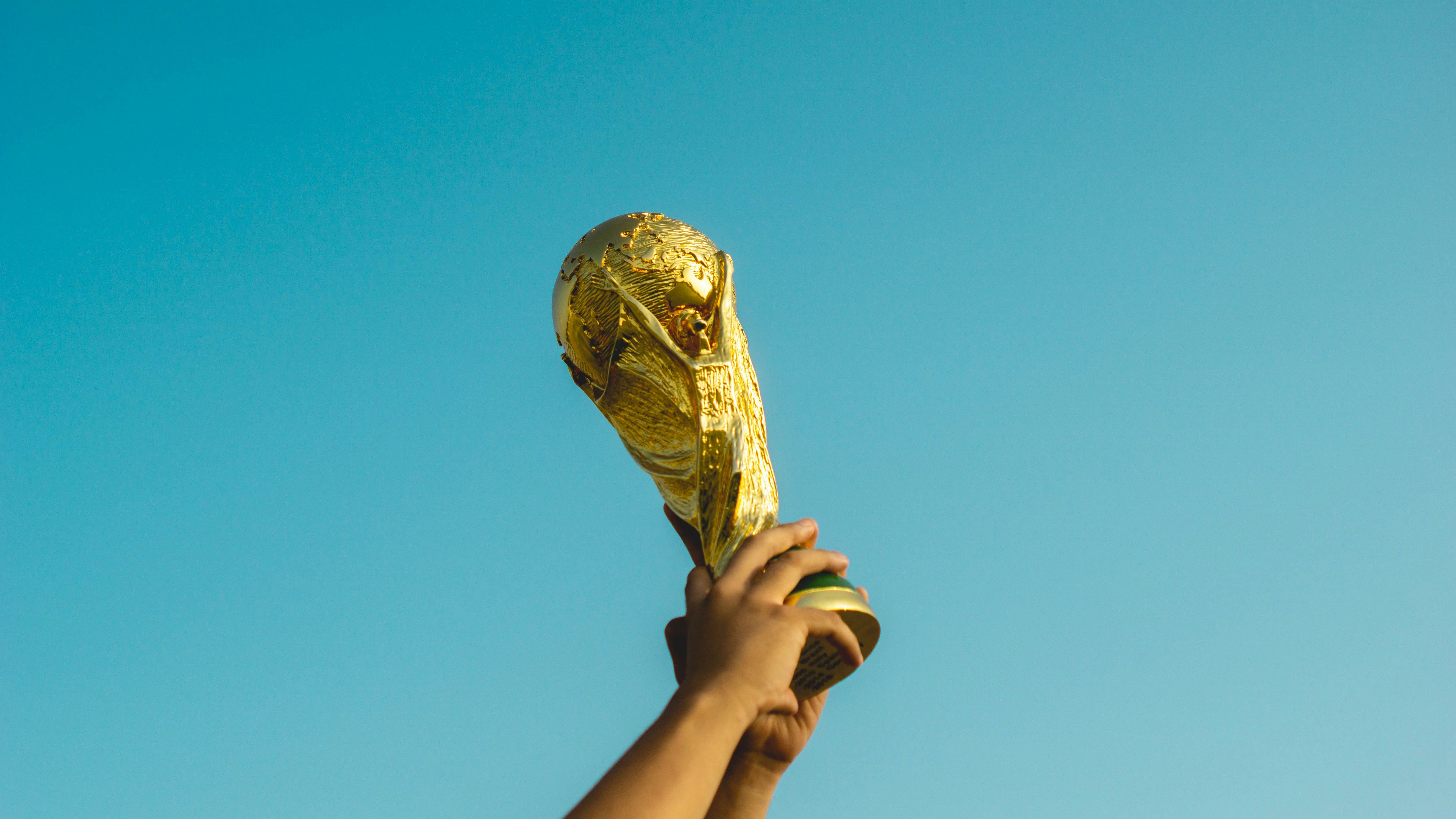A hand holding the FIFA World Cup trophy aloft against a clear blue sky