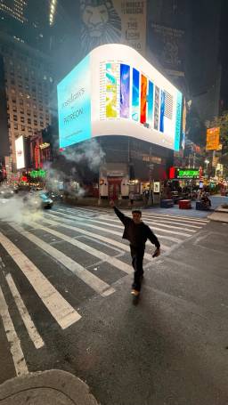 Ross standing in the street, pointing at the billboard at night.