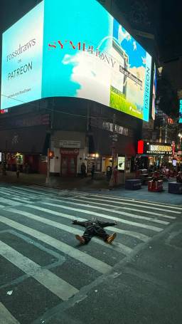 Ross lying in the street in front of the billboard at night.