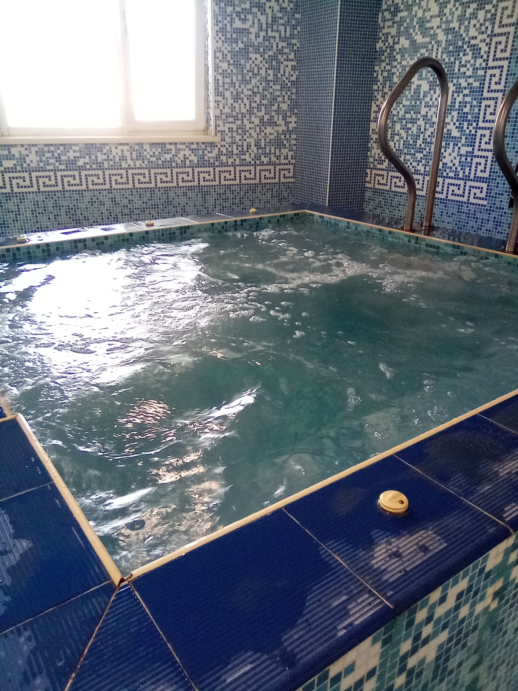 Bubbling indoor jacuzzi with blue mosaic tiles and metal handrails