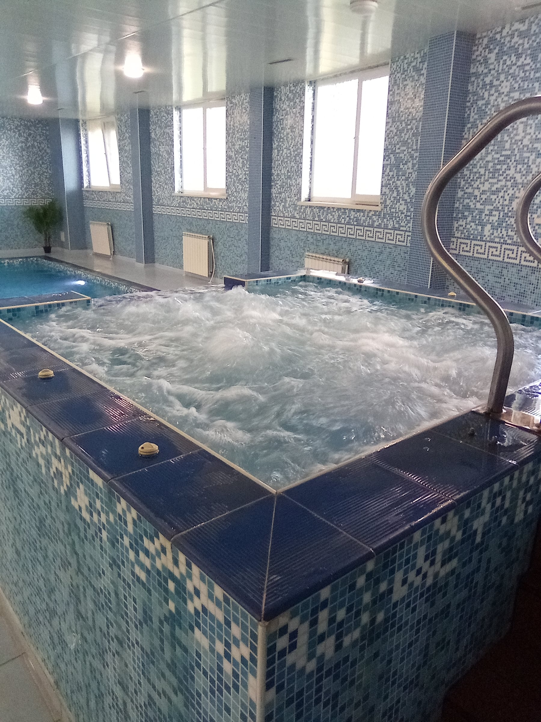 Raised indoor jacuzzi with bubbling water beside the pool, large windows behind