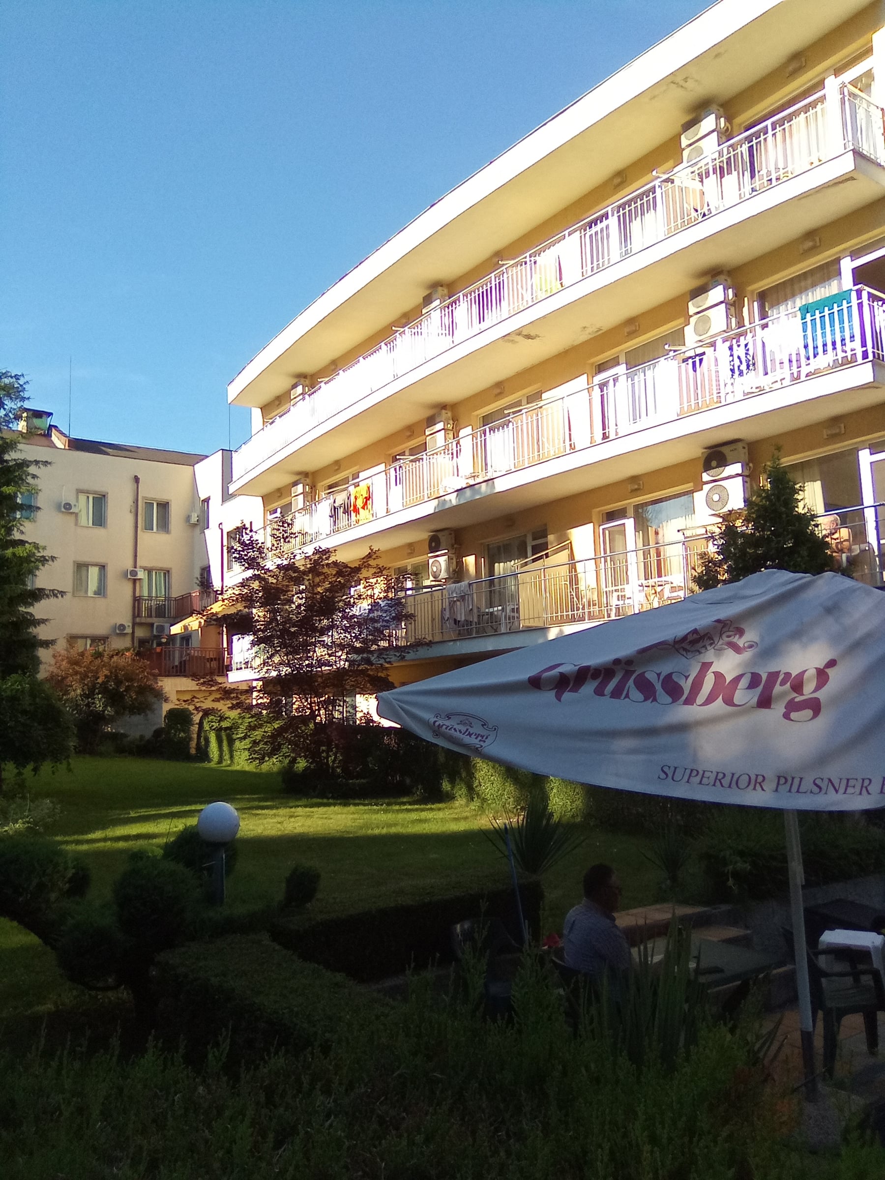 Multi-storey hotel building with balconies above a garden with a parasol