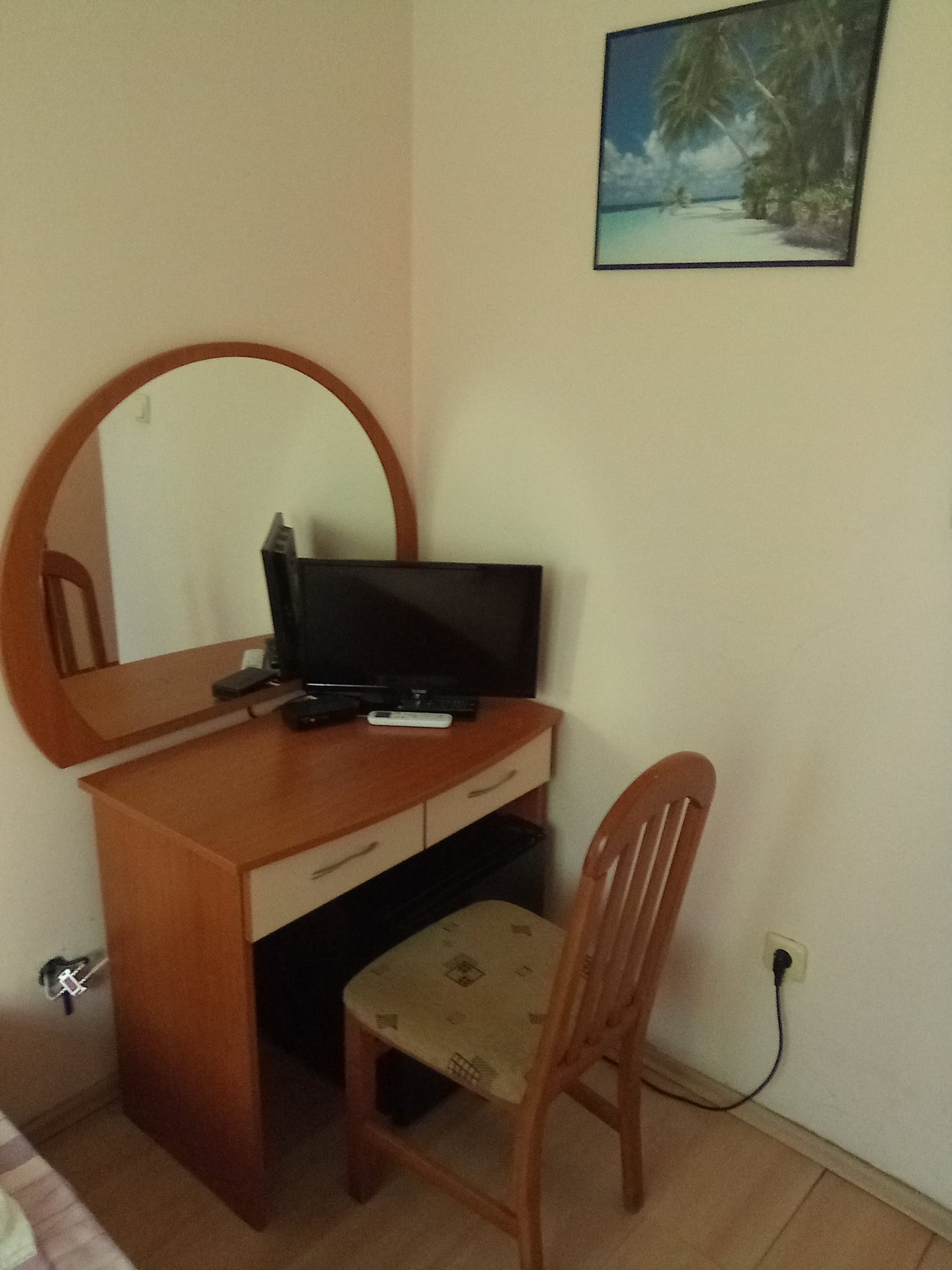 Wooden desk with a round mirror, a small TV and a chair in a hotel room