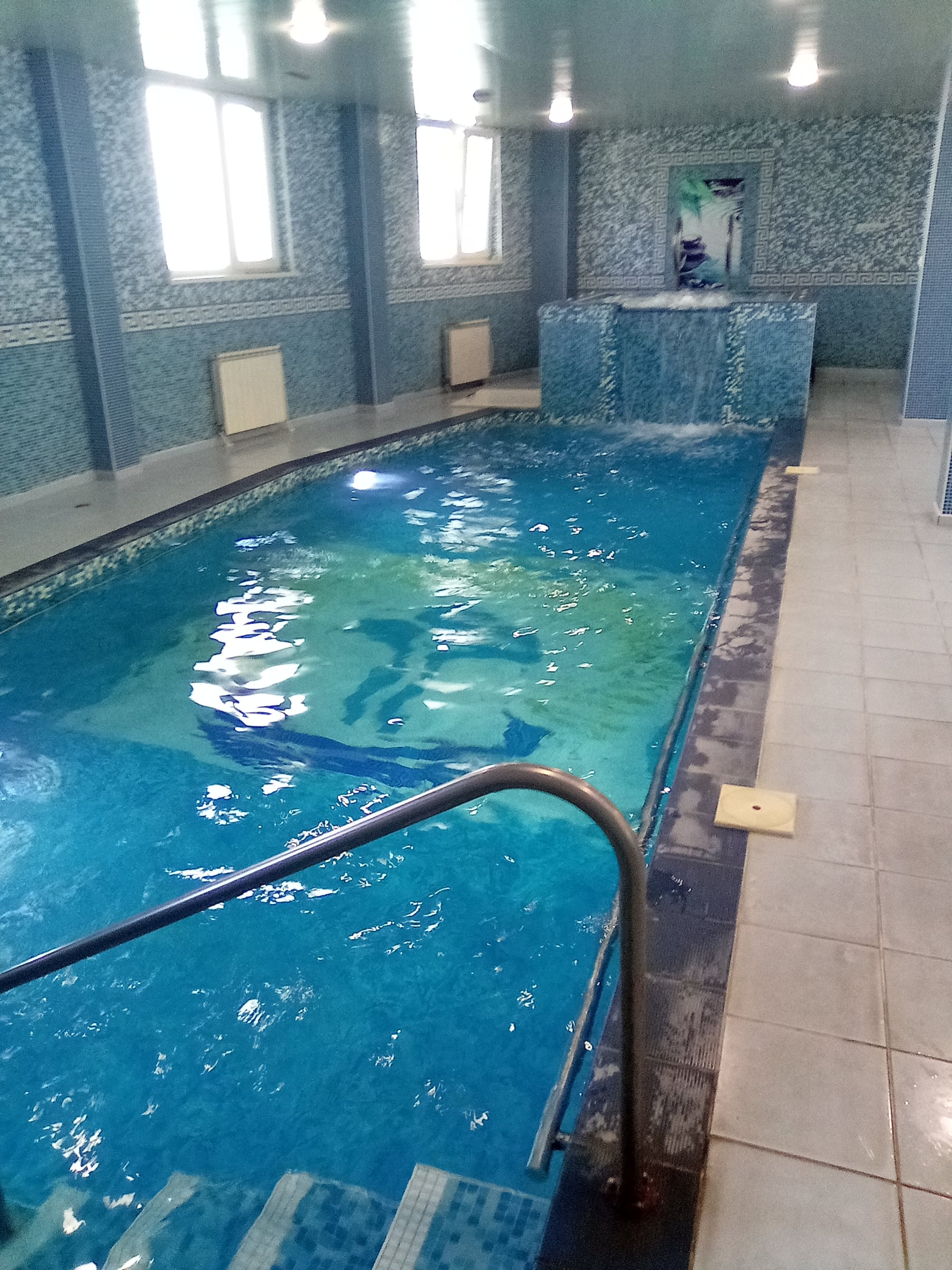 Indoor pool with a handrail and steps, a raised jacuzzi visible in the background