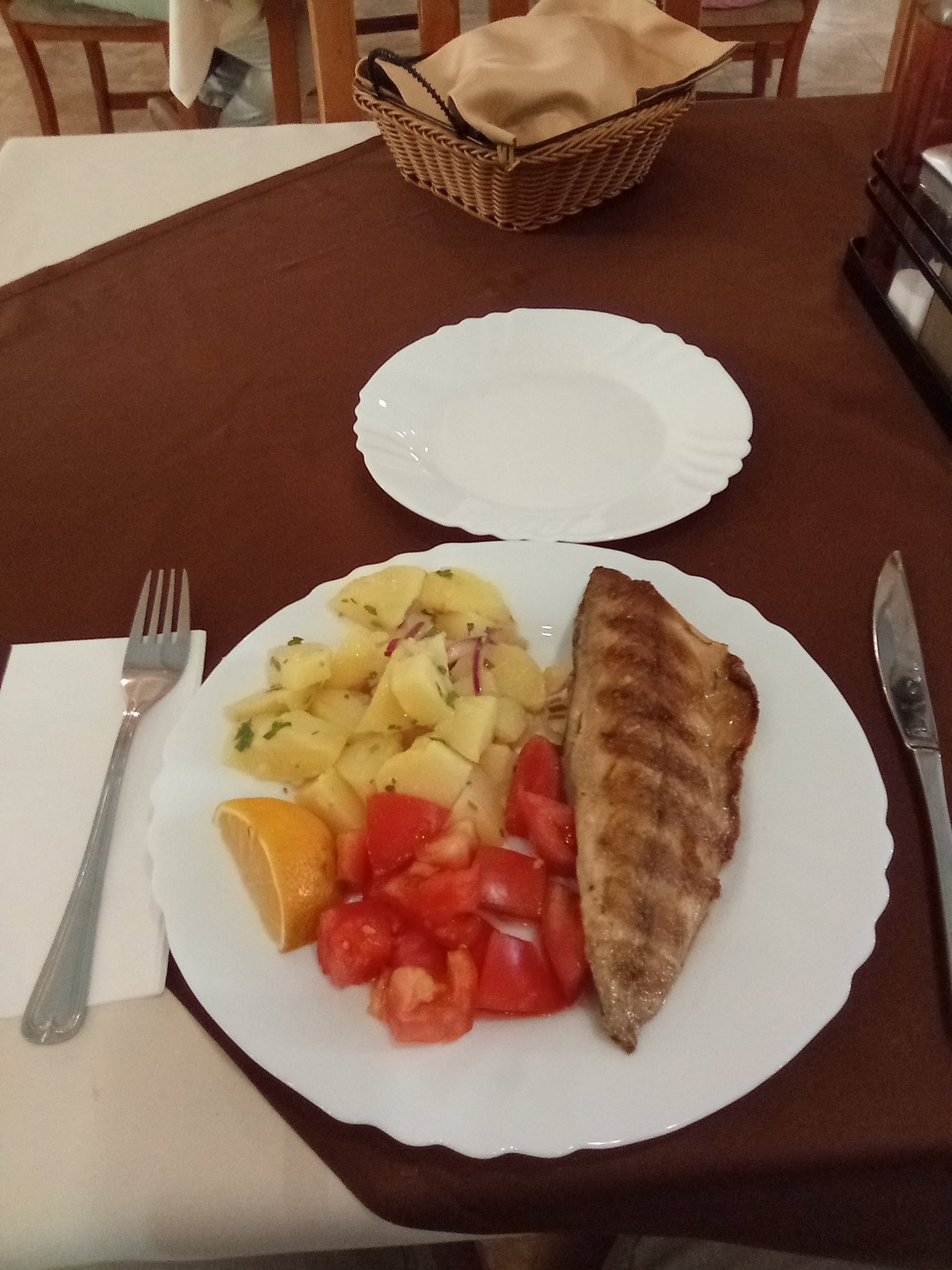 Plate of grilled fish, boiled potatoes, tomatoes and an orange slice on a restaurant table
