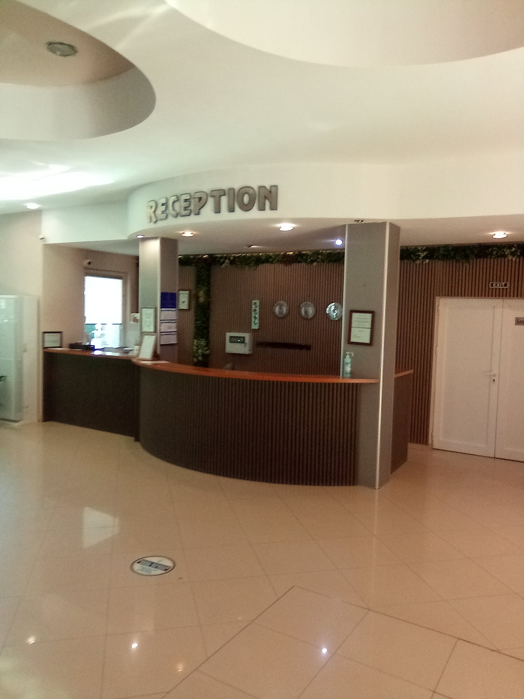 Hotel reception desk under a "Reception" sign in a light lobby with a tiled floor