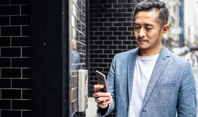 man outside building holding phone next to access reader
