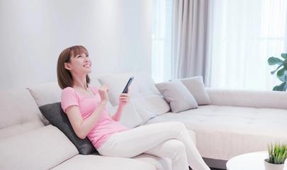 Woman sitting on couch uses smartphone to control smart home devices