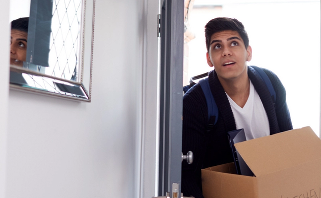 College student enters his apartment with a moving box