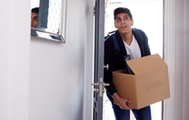 College student enters his apartment with a moving box